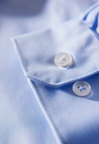 Lichtblauwe shirt met een gladde textuur, voorzien van een omgeklapte kraag en twee doorzichtige plastic knopen met blauwe stiksel.