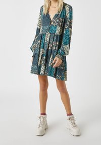 Robe à manches longues avec un design en patchwork dans des motifs en bleu canard, floraux et à pois. Tissu à la texture douce, avec un détail boutonné.