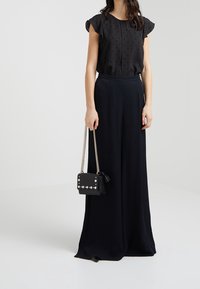 Svart blus med prickmönster, fjärilsmanschetter, kombinerad med vida svarta byxor. Liten svart handväska med nitar och kedjerygg.