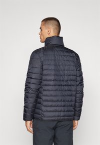 Marineblaue Steppjacke mit horizontalem Quilt-Design, hohem Kragen und langen Ärmeln. Glatte Textur und dezentes Logo-Detail auf der Schulter.
