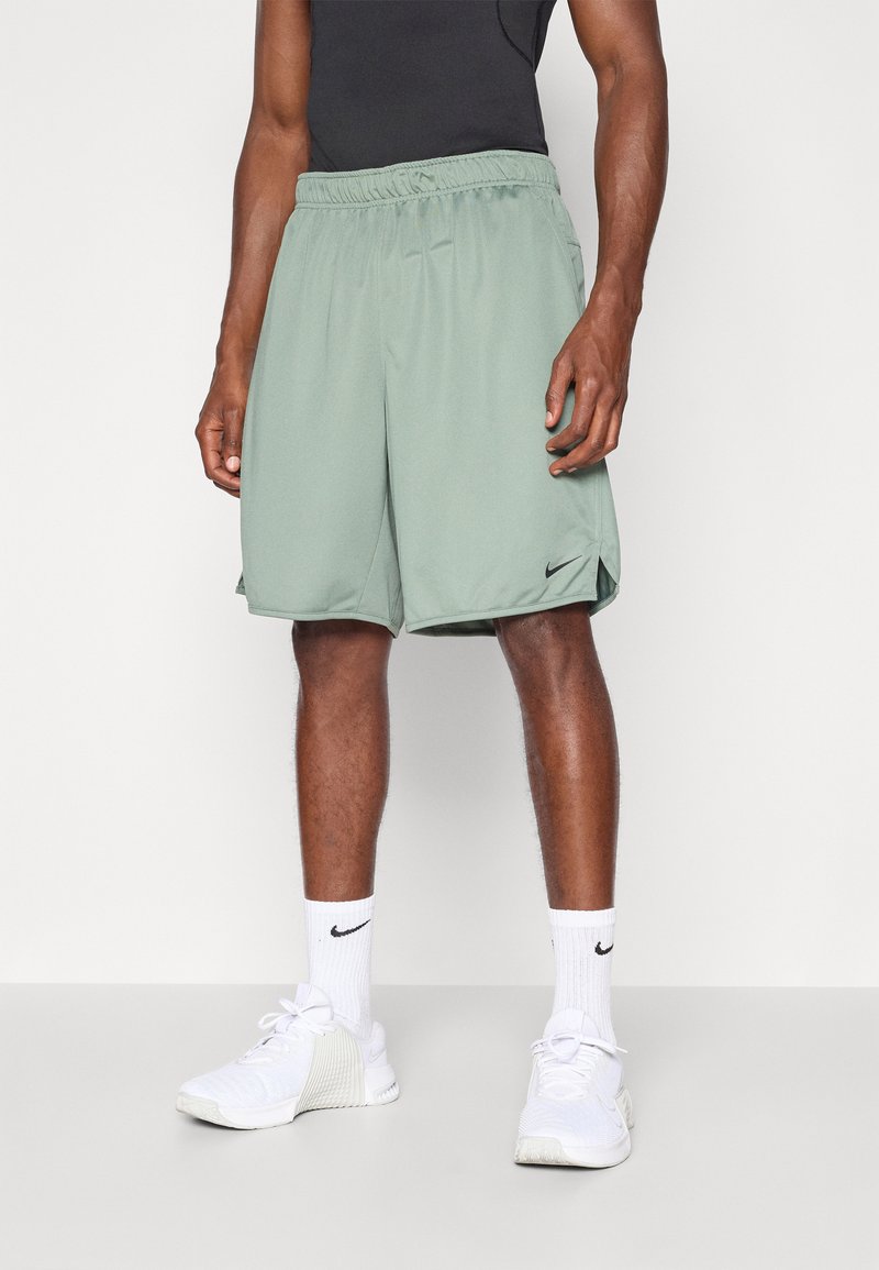 Grüne Sportshorts mit elastischem Bund und seitlichen Schlitzen, aus leichtem Material, kombiniert mit weißen Sneakers und Socken.
