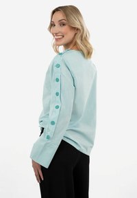 Camicia di corduroy turchese chiaro con taglio dritto, caratterizzata da dettagli con bottoni lungo le maniche, maniche lunghe e vestibilità rilassata.