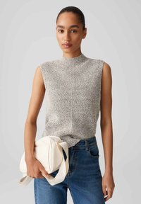 Light gray sleeveless knit top with a high neckline, featuring a textured pattern, paired with dark blue jeans and a white shoulder bag.