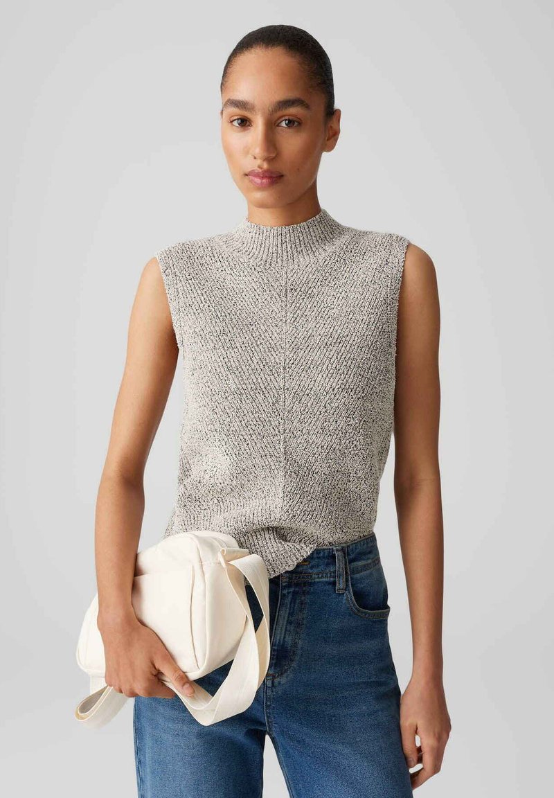 Light gray sleeveless knit top with a high neckline, featuring a textured pattern, paired with dark blue jeans and a white shoulder bag.
