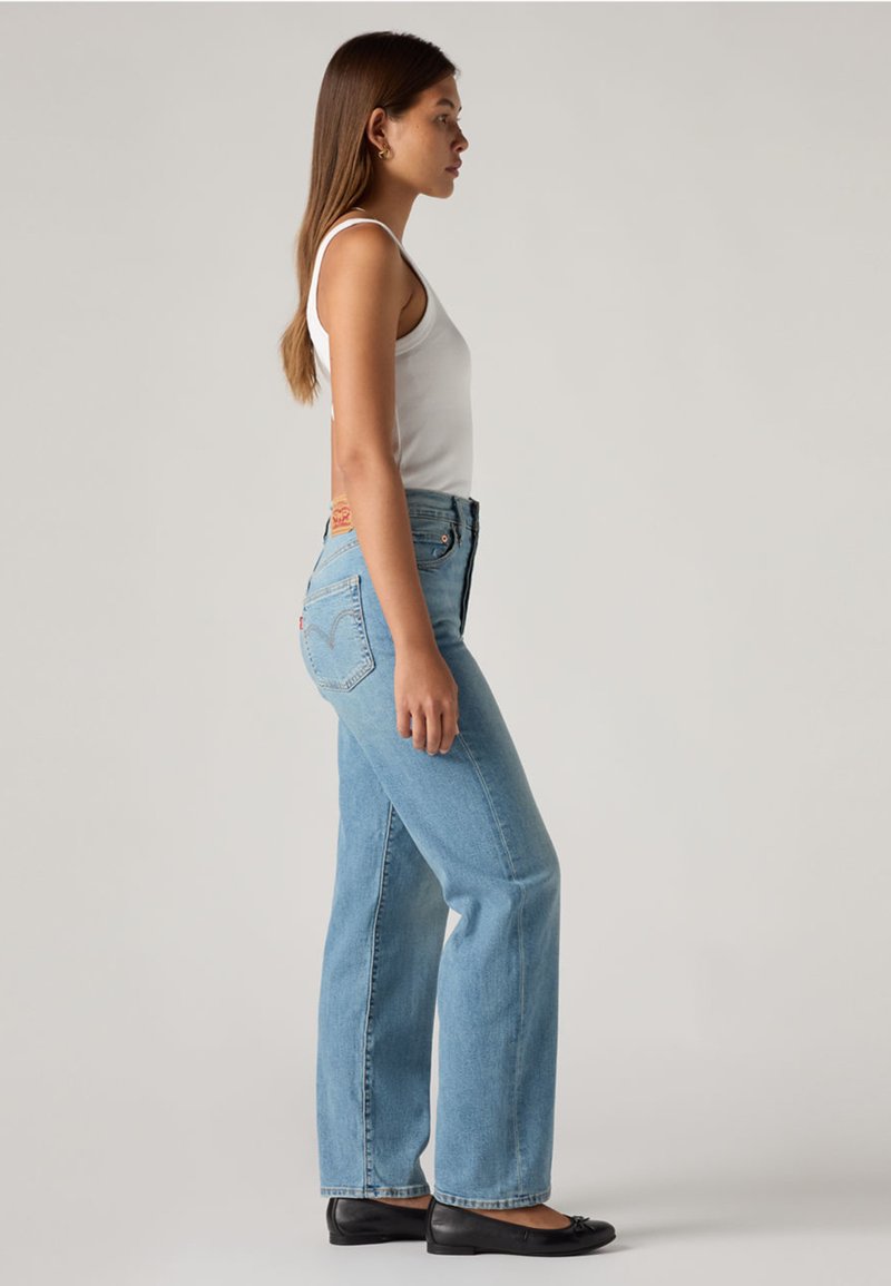 Jeans azzurri chiaro a vita alta con vestibilità rilassata, design a cinque tasche e dettagli di cuciture sottili. Abbinati a un top bianco senza maniche e ballerine nere.