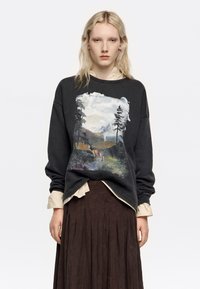 Sudadera negra con un gráfico de temática natural que presenta montañas, árboles y un ciervo. Tejido ligero, corte holgado, puños y cuello acanalados.