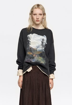 Czarna bluza z grafiką w tematyce natury przedstawiającą góry, drzewa i jelenia. Lekka tkanina, luźny krój, ściągacze przy mankietach i dekolcie.