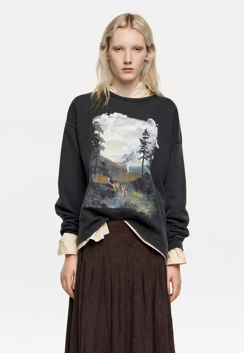 Sudadera negra con un gráfico de temática natural que presenta montañas, árboles y un ciervo. Tejido ligero, corte holgado, puños y cuello acanalados.