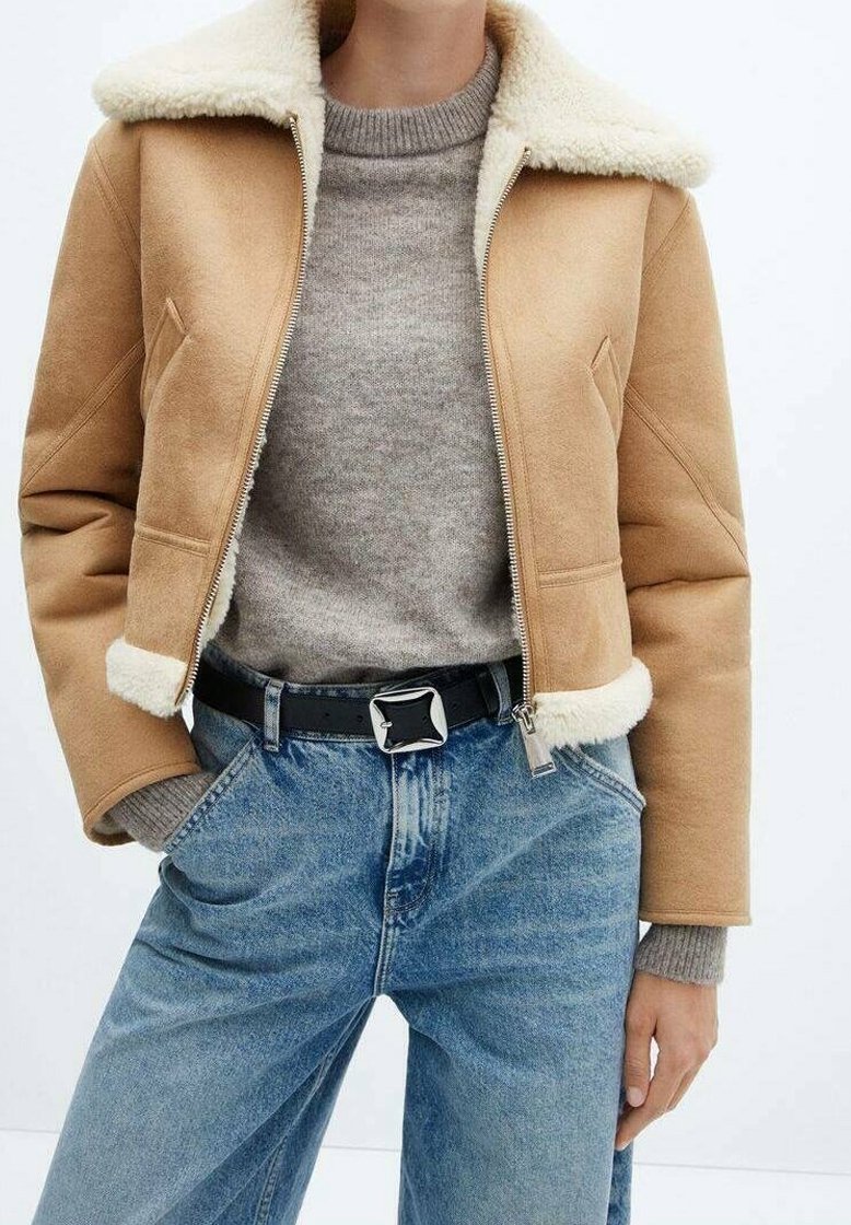 Veste courte camel avec col en peau lainée, portée avec un pull gris clair, un jean en denim bleu et une ceinture noire avec une boucle carrée argentée.