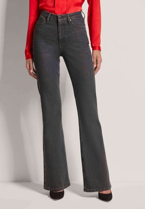Flared black jeans with a high waist and faded texture, paired with a red shirt and black heels, displayed against a neutral background.