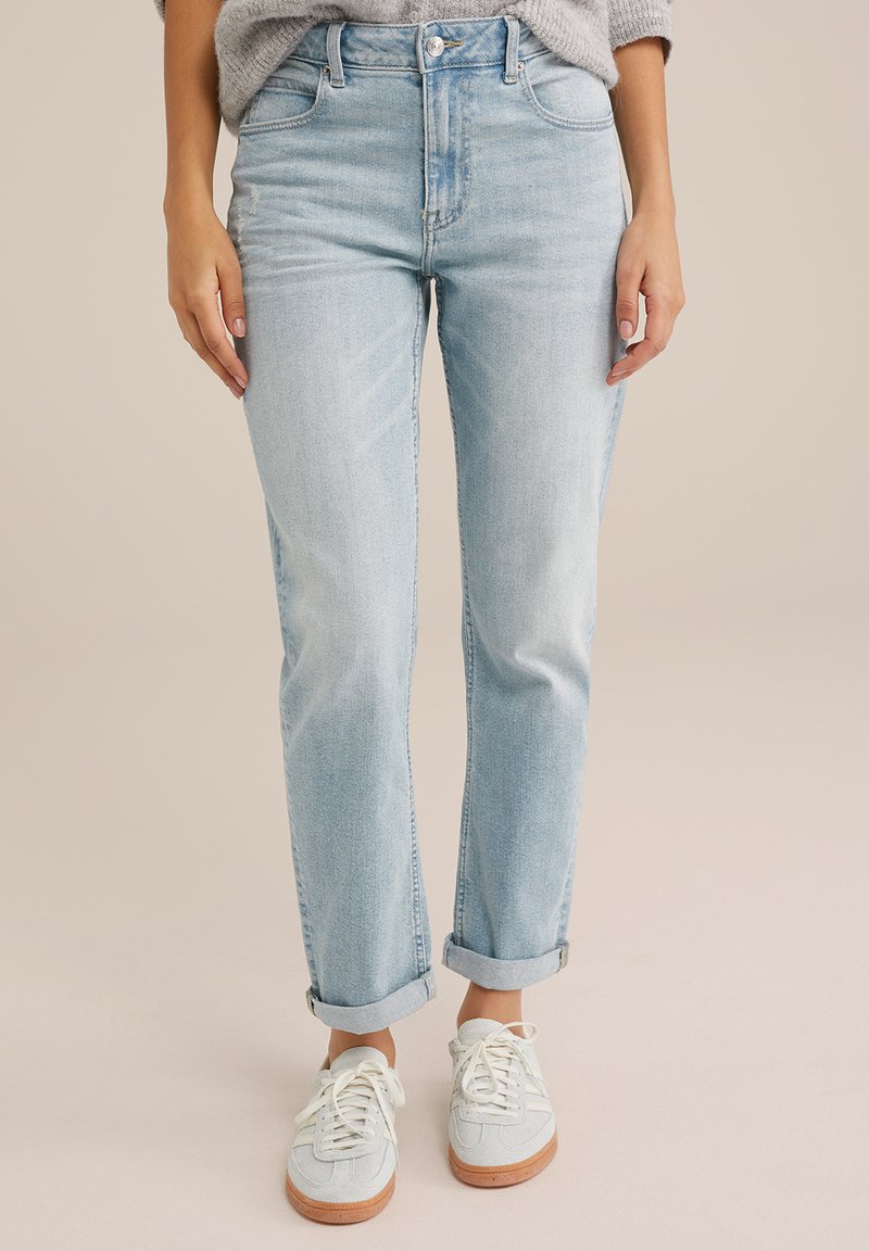 Ljust blå, högmidjade jeans med rak benform, rullade manschetter och subtila blekningar. Kombination med ljusa sneakers.