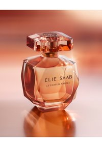 Klart glass parfymeflaske med geometrisk form, rosagullfarge og sekskantet lokk; har svart tekst "ELIE SAAB LE PARFUM ABSOLU."