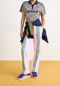 Blommönstrad polo med marinblå krage, tillsammans med rosa träningbyxor med gröna ränder. Tillbehören inkluderar en marinblå jacka knuten runt midjan.