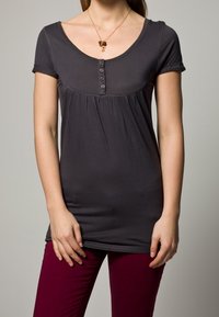 Grå kortärmad t-shirt med rundad hals, fyra knappar framtill och rynkdetaljer nedanför bysten, som matchas med burgundyfärgade byxor.