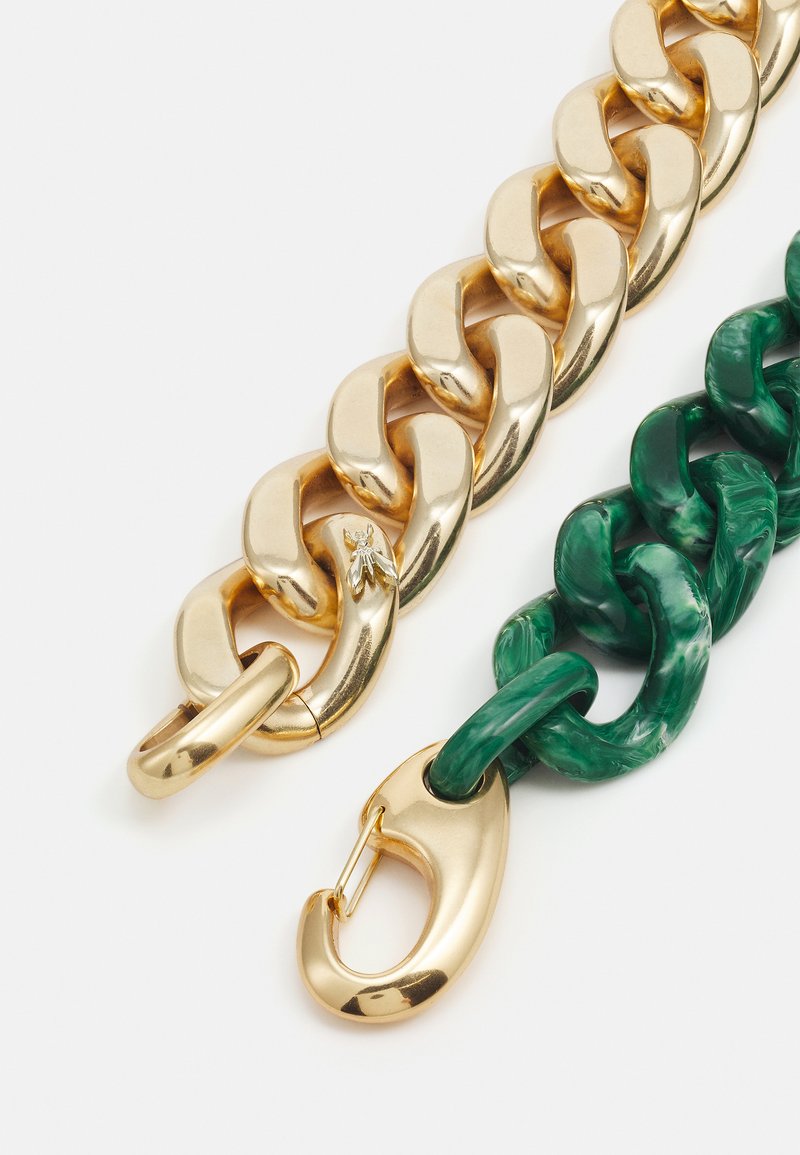Goldene Metallkette mit polierter Oberfläche, kombiniert mit einer grün marmorierten Kette. Bemerkenswerte Hardware umfasst einen goldenen Verschluss und ein dekoratives Element.