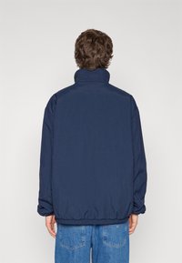 Giacca a vento blu navy con colletto alto, polsini elasticizzati e orlo con cordino. Tessuto liscio con un design elegante e casual.