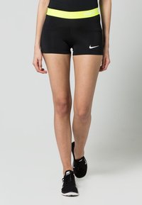 Svarta idrottsshorts med ett högt gult midjeband som har logotypen. Tyget är slätt och åtsittande, utformat för aktiv användning.