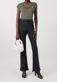 Top a maniche corte a righe verdi e nere abbinato a pantaloni neri a zampa in tessuto a coste. Accessoriato con una borsa a tracolla bianca trapuntata e sandali viola con tacco.