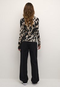 Haut à manches longues beige avec imprimé animal noir, associé à un pantalon large noir. Le tissu semble doux, avec une texture lisse.