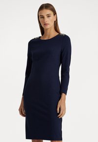 Rochie din bumbac de culoare bleumarin, cu mâneci lungi, decolteu rotund și nasturi aurii pe umeri. Textură netedă și tăietură până la genunchi.
