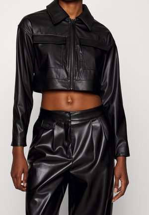 Veste courte en similicuir noir avec fermeture éclair devant et poches à rabat, associée à un pantalon plissé en similicuir noir taille haute.