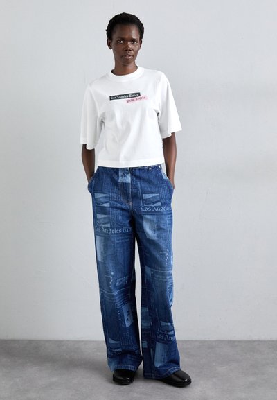 White cropped t-shirt with graphic text; high-waisted wide-leg jeans in blue denim with newspaper pattern details. Black shoes.