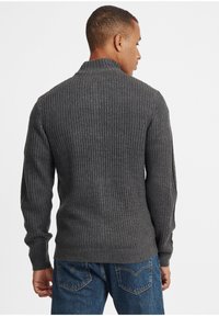 Grå strikkegenser med høy krage, preget av ribbestruktur og lange ermer, sammen med blå denimjeans.