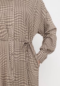 Long-sleeve button-up shirt in houndstooth pattern, featuring a tie waist and pockets. Made of lightweight, textured fabric in neutral tones.