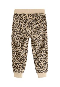 Beige fleecebukser med sort leopardprint, der har elastisk talje og ribbede manchetter ved anklerne. Blød tekstur, afslappet design.