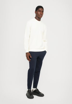 Light cream sweatshirt with a round neck and a chest pocket, paired with navy tapered pants. Black sneakers complete the outfit.