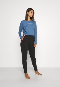 Camisa de manga larga azul con el logo "TOMMY HILFIGER"; pantalones jogger negros con rayas laterales rojas y blancas y bolsillos laterales.