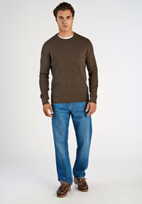 Suéter marrón de canalé con cuello redondo, combinado con jeans rectos azules y zapatos de barco marrones con cordones. Atuendo simple y casual.