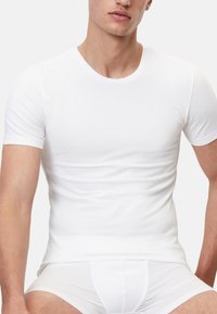 Hvid, kortærmet T-shirt lavet af glat stof, tætsiddende design der omfavner kroppen. Har en klassisk rund halsudskæring og sømløs konstruktion.
