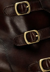 Bota de cuero marrón con tres correas ajustables y hebillas doradas. La textura es suave con detalles de costura visibles.