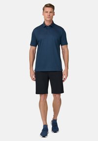 Polo blu navy con colletto classico, maniche corte e vestibilità ampia, abbinata a pantaloncini neri e scarpe da ginnastica blu.