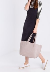 Szara torba tote z długimi uchwytami, wykonana z gładkiego materiału, prostokątna w kształcie, zestawiona z czarną sukienką i białymi butami na slip-on.