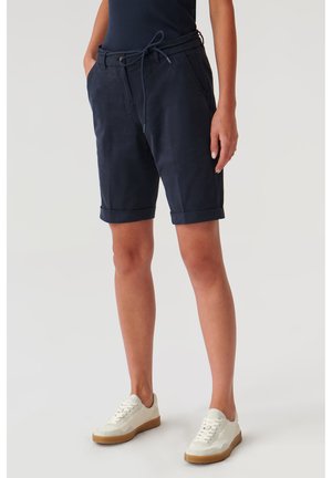 Marineblå dameshorts lavet af letvægtsstof, med en snøre i taljen, op-rullede manchetter og sidelommer; parret med hvide sneakers.