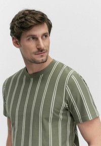 Olijfgroene T-shirt met korte mouwen, voorzien van witte verticale strepen, een ronde halslijn en een textuurstof. Eenvoudig ontwerp zonder extra accenten.