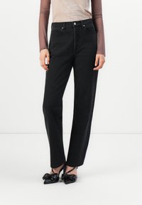 Black high-waisted jeans with a straight leg silhouette, made from denim; features front pockets and a raw hem. Paired with black heels.