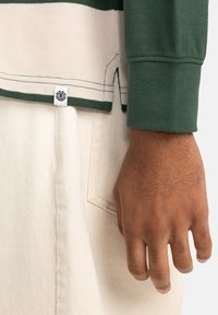 Green long-sleeve shirt with horizontal cream stripes, featuring a textured fabric and side slits. Includes a small label at the hem.