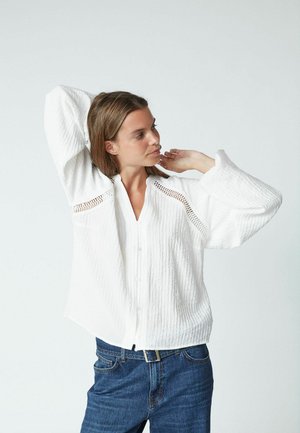 White button-up shirt with textured fabric, featuring openwork detailing on the sleeves and a relaxed fit. Worn with dark blue denim jeans.