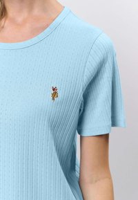 Svetlomodrá rebrovaná krátky rukávová košeľa s malým vyšívaným logom jazdca na koni na ľavej strane hrudníka.