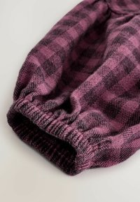 Tissu à carreaux violets et noirs avec poignet élastique, mettant en valeur une texture douce et un motif tissé. Bords arrondis avec un détail de finition froncé.