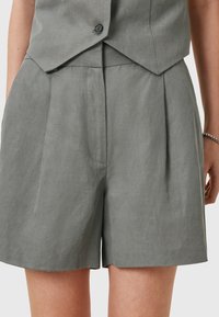 Pantaloni corti di lino grigi con pieghe e una vestibilità rilassata. Presentano un fronte piatto e tasche laterali, tessuto testurizzato e lunghezza fino alla coscia.