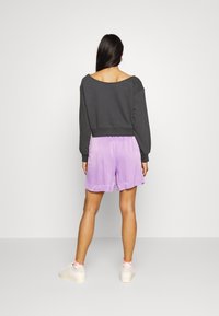 Sweatshirt cinza escuro, design fora do ombro. Combinado com calções de cetim lilás claros, com faixa elástica na cintura e textura suave.