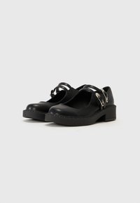 Black leather shoes with a rounded toe, ankle straps, and a chunky heel. Features silver hardware accents and a stitched sole.