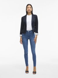 Jūrinio stiliaus švarkas su juostelėmis ant rankovių, balta marškinėliai ir mėlynos liesos džinsai. Juodi atviri kulniukai. Dėmesys pritaikytam silueto modeliavimui ir kontrastingoms tekstūroms.