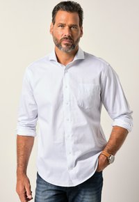 Camisa blanca de botones con un pequeño patrón de puntos azules, mangas largas arremangadas hasta los codos, bolsillo frontal, combinada con jeans oscuros y un reloj.