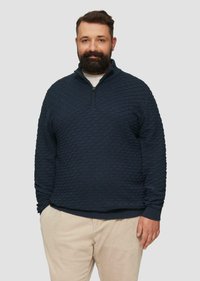 Marineblauwe gebreide pullover met een ruitpatroon, kwart-rits kraag en geribde manchetten, gecombineerd met lichtgekleurde corduroy broeken.