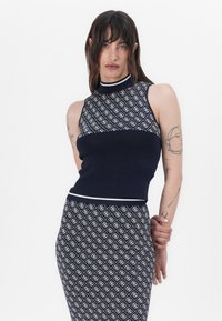Top senza maniche blu navy con collo alto, caratterizzato da un motivo geometrico bianco, abbinato a una gonna aderente coordinata che presenta lo stesso design.